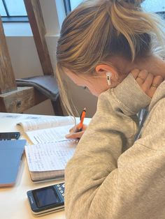 a woman sitting at a table writing on a piece of paper with a pen in her hand