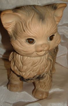 a ceramic cat figurine sitting on top of a white cloth covered tablecloth