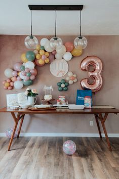 a birthday party with balloons and decorations on the wall above a wooden table in front of a large number 3 balloon