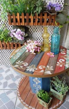 a colorful table with flowers and vases on it in front of a white fence