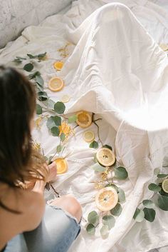 a woman sitting on top of a bed covered in lemons and eucalyptus leaves next to a white blanket