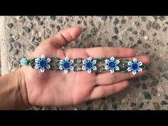 a hand holding a beaded bracelet with blue and green flowers on it's side