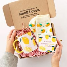 someone is holding a box with two mugs in it and some lemons on them