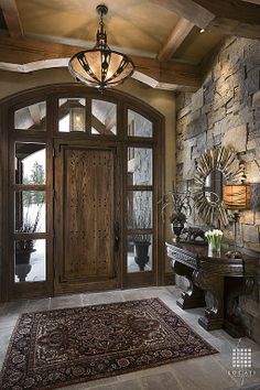 a foyer with stone wall and wooden door, rug on the floor and chandelier