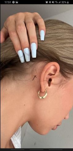 a woman's ear with white acrylic nails and a gold hoop piercing