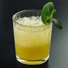 a close up of a drink in a glass on a black table with a mint garnish