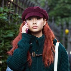 a woman with red hair is talking on her cell phone while wearing a green sweater