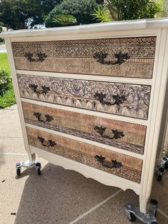 an old dresser is painted white and has intricate designs on the drawers, as well as wheels