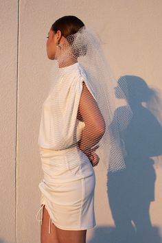 a woman wearing a white dress and veil standing in front of a wall with her hands on her hips