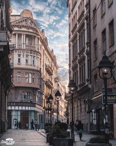 people are walking down the street in an old european city with tall buildings on either side