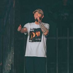 a man standing on top of a stage holding a microphone in his hand and wearing a hat