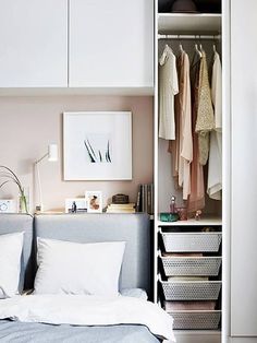 a bedroom with white cabinets and clothes hanging on the wall next to it's bed