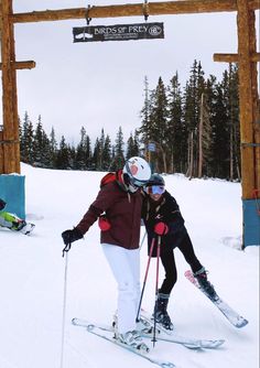 two people on skis pose for a photo under the sign at the top of a mountain