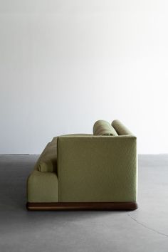 a green couch sitting on top of a floor next to a white wall in an empty room