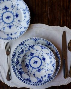 a blue and white dinner set with silverware on a wooden tablecloth, next to a fork and knife