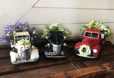 three old fashioned cars with flowers in them are sitting on a wooden shelf next to a wall