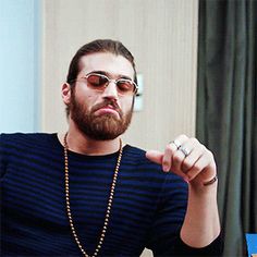 a man with a beard wearing sunglasses pointing to the side while sitting at a table