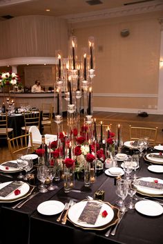 the table is set with black linens, white plates and red roses in tall glass vases