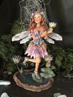 a fairy figurine holding flowers on top of a rock