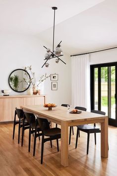 a dining room table with black chairs and an oval mirror on the wall above it