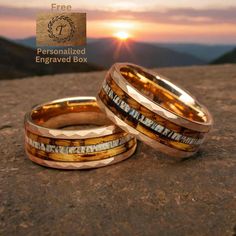 two gold wedding bands sitting on top of a rock with the sun setting in the background