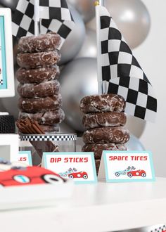 a table topped with donuts covered in frosting next to race flags and balloons