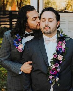 two men in tuxedos kissing each other with flowers on their lapel collars