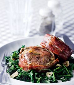 two meats are on top of greens in a white bowl with silverware next to it