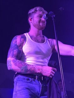 a man standing in front of a microphone with tattoos on his arm and chest,