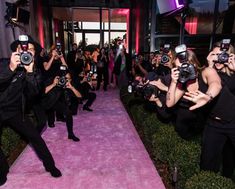 a group of people with cameras taking pictures on the pink carpet at a fashion show