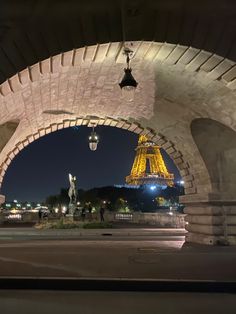 the eiffel tower is lit up at night from under an arched stone bridge