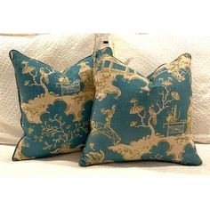 two blue and gold pillows sitting on top of a white couch next to each other