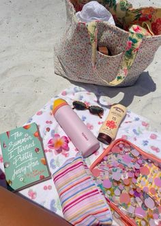 the contents of a beach bag are laid out on the sand