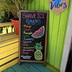 a chalkboard sign sitting on the side of a green wooden wall next to a potted plant