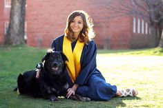 a woman sitting on the grass with her dog wearing a graduation gown and smiling at the camera