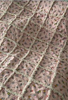 a pink quilt with white ruffles and flowers on the bottom is laying on top of a bed