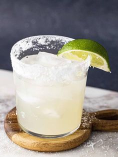 a margarita sitting on top of a wooden cutting board next to a slice of lime