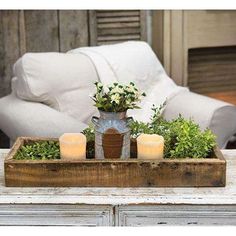 a wooden tray with candles and flowers in it sitting on a table next to a couch