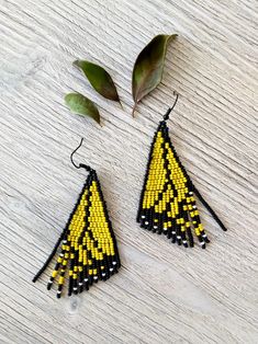 yellow and black beaded triangle earrings on white wooden table with green leaves next to it