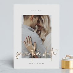 save the date card with gold foil lettering on it and a ring next to it