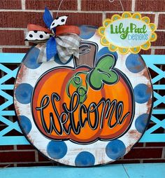 a wooden sign with the word welcome painted on it and a polka dot bow hangs from a brick wall