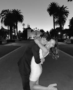 a man and woman hugging each other on the sidewalk with palm trees in the background