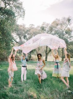 four young women are playing with an umbrella in the grass while one woman is holding up her veil