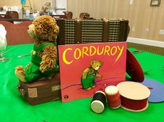 a teddy bear sitting on top of a suitcase next to a sign that says corduroy