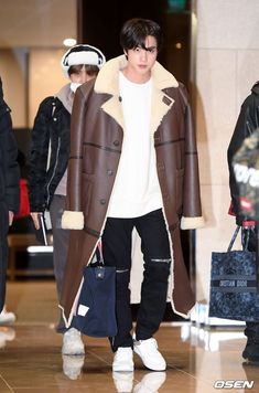 a man in a brown coat is walking through an airport