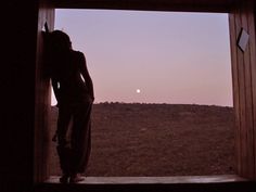 a woman standing in front of a window with the moon behind her and looking out