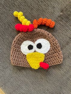 a crocheted turkey hat is shown on top of a gray chair with an orange nose