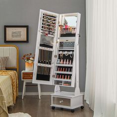 a white jewelry cabinet sitting on top of a hard wood floor next to a bed