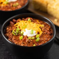 two black bowls filled with chili and cheese