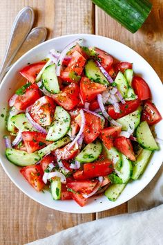 a white bowl filled with cucumber and tomato salad next to two spoons